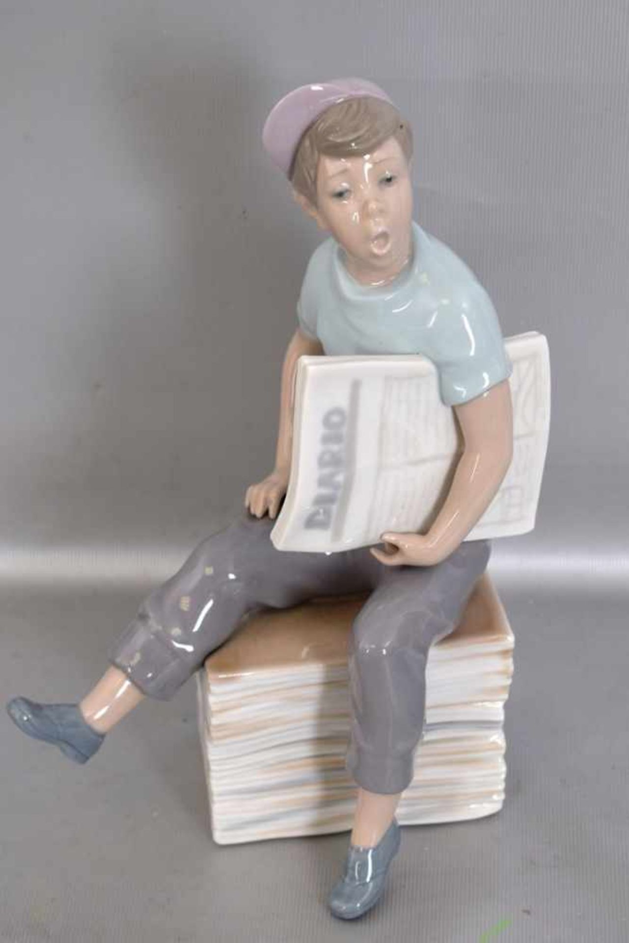 Der Zeitungsjunge auf Zeitungsstapel sitzend, Knabe mit Mütze und Zeitung, bunt bemalt, H 23 cm, FM