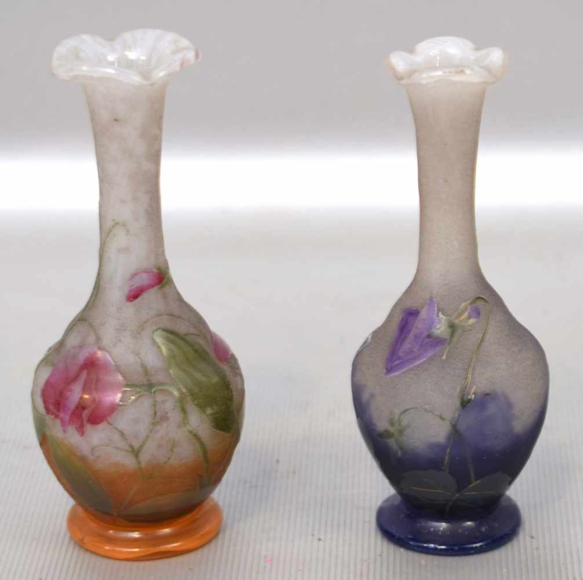 Zwei ZiervasenMilchglas, runder Fuß, Wandung leicht gebaucht, mit lila bzw. rosa aufgelegten Blüten,