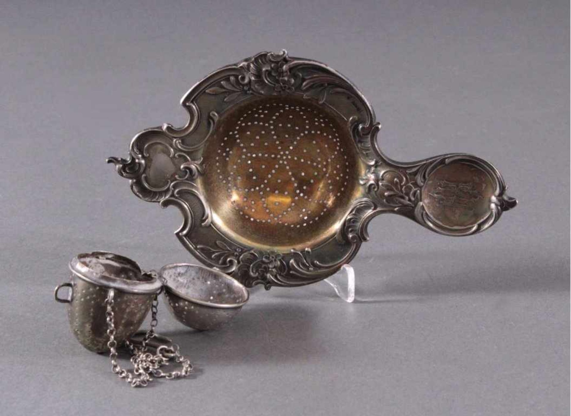 Silbernes Teesieb und Tee-EiReliefiertes Sieb, innen vergoldet, am Griff mit MonogrammCH, punziert