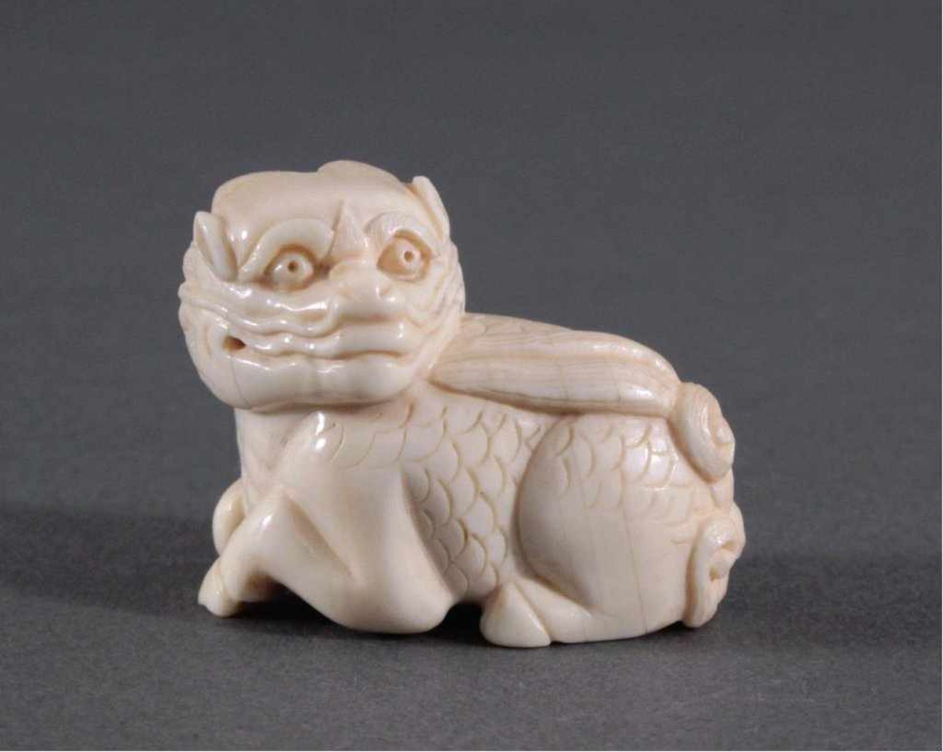 Netsuke, Japan 1. Hälfte 20. Jh., Elfenbein geschnitztLiegender Drache, signiert, ca. 3,4 x 4,1 x