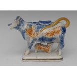 A Pratt Ware cow creamer and cover, the cow stands sponged in blue and tan, downward horns,