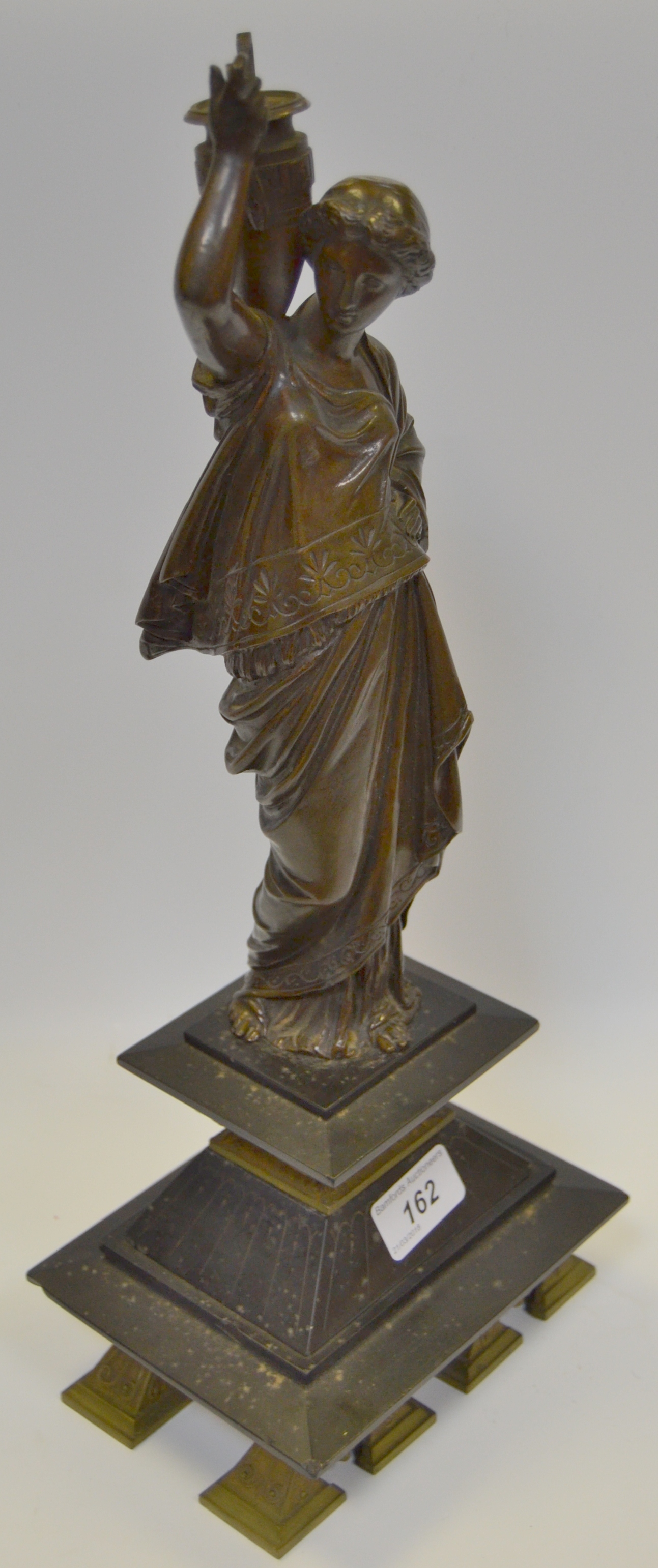 An early 20th century bronze figure of a Woman dressed in robes carrying a twin handled urn,