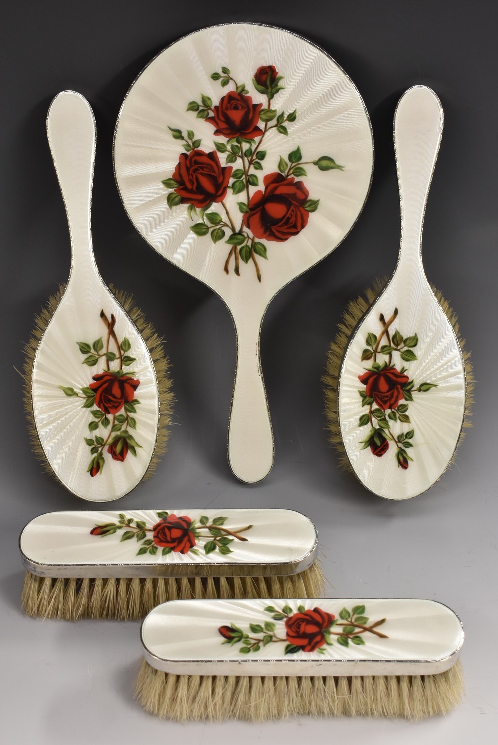 An Elizabeth II silver and enamel five piece dressing table set, comprising a hand mirror,