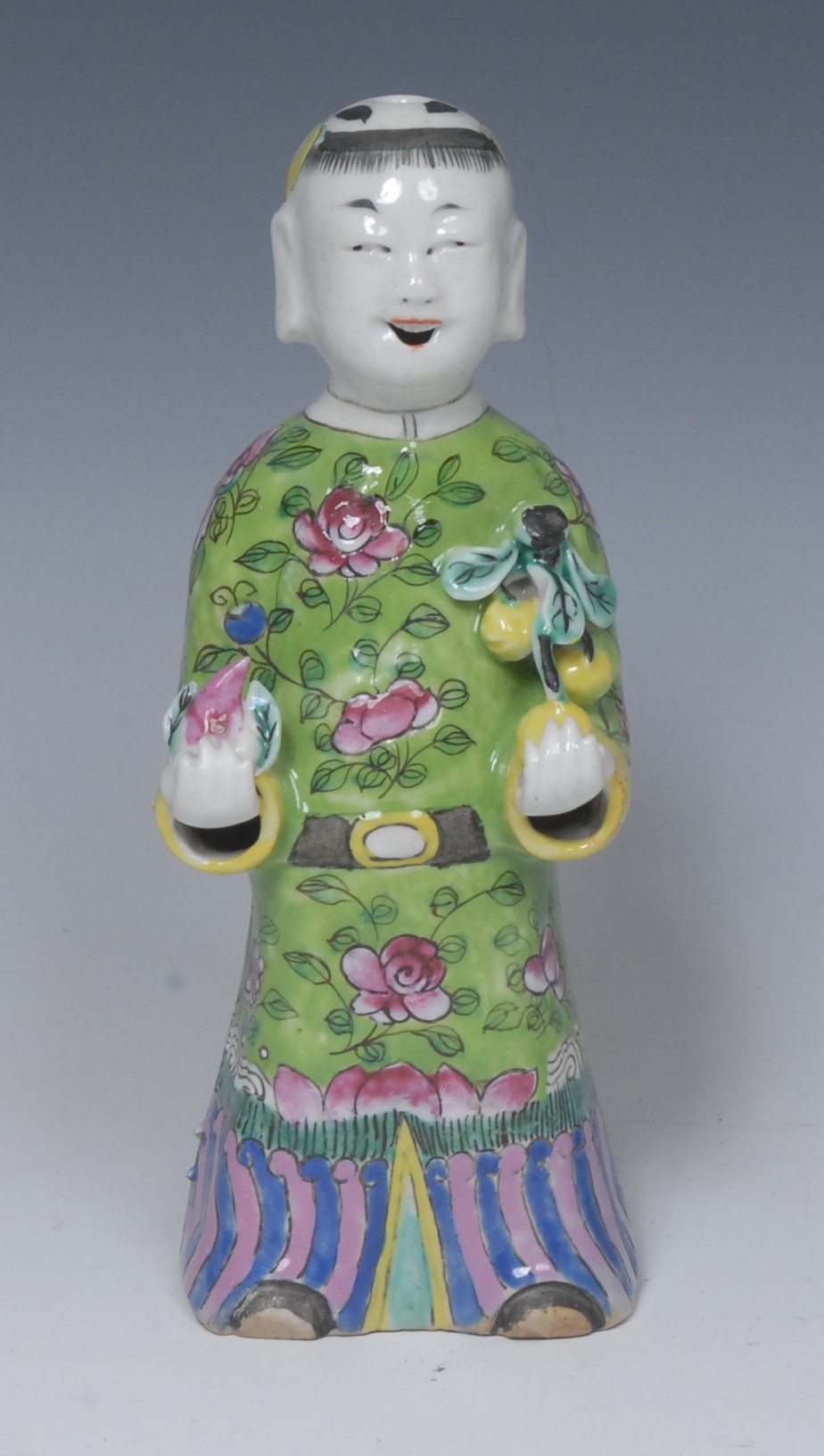 A Chinese figure, of a boy holding a lotus and peach blossom, 19cm high,