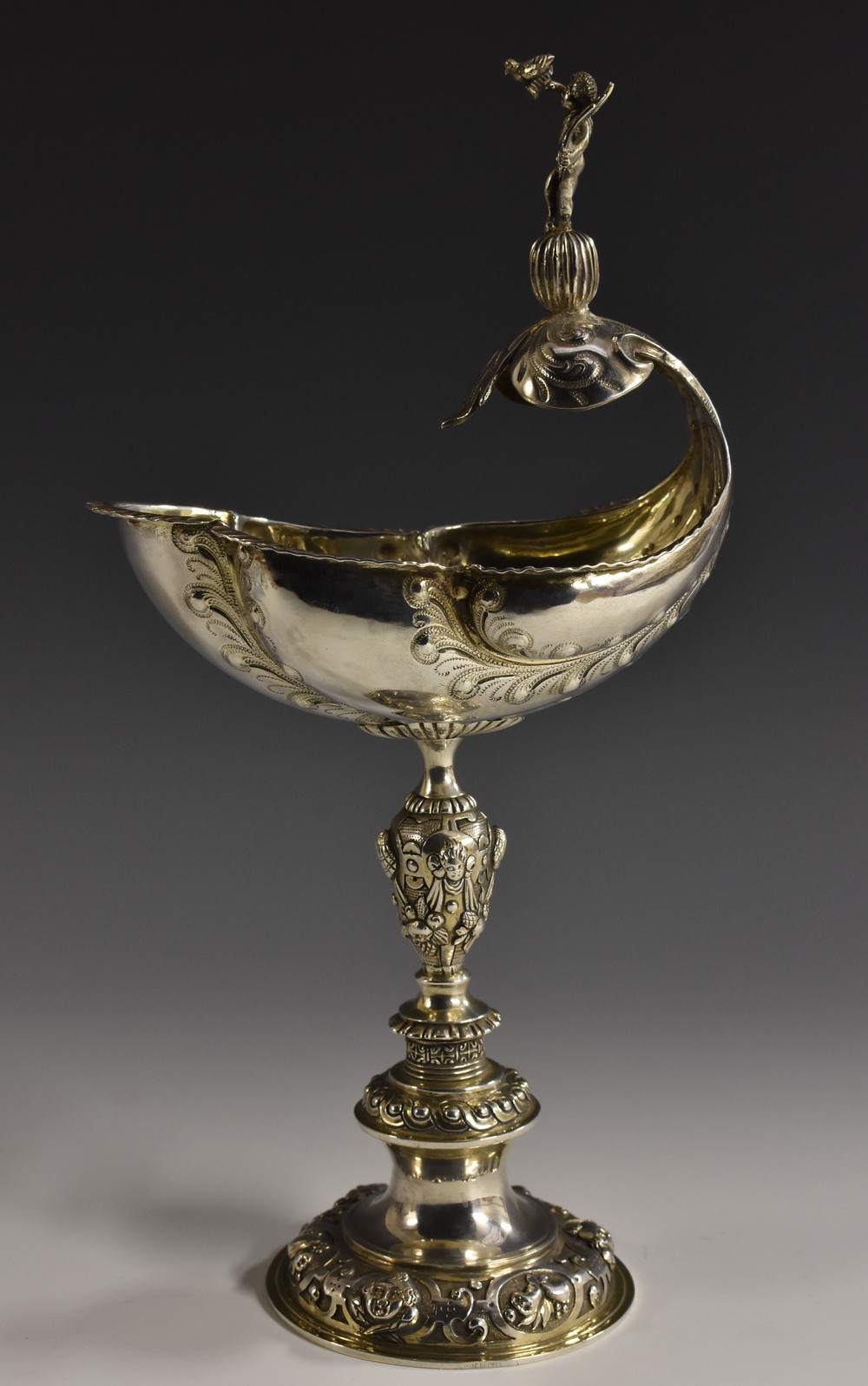 An Edwardian Historicist silver copy of an Elizabethan shell cup, crested by a scantily clad putto,