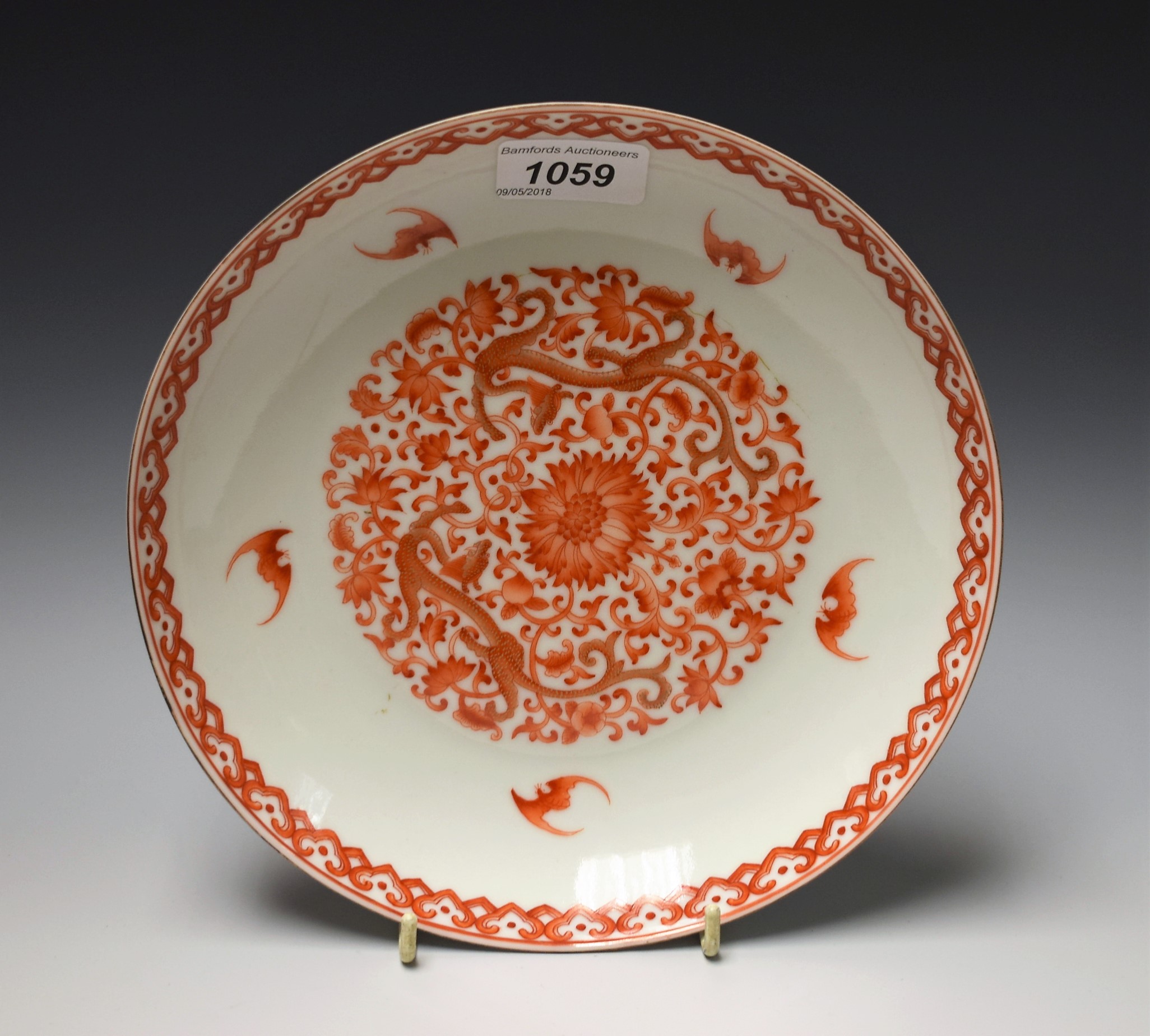 A Chinese dish, decorated in in red with lotus and scrolling foliage, the rim with bats,