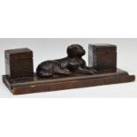 A late 19th century Black Forest two well standish, carved with a recumbent hound,