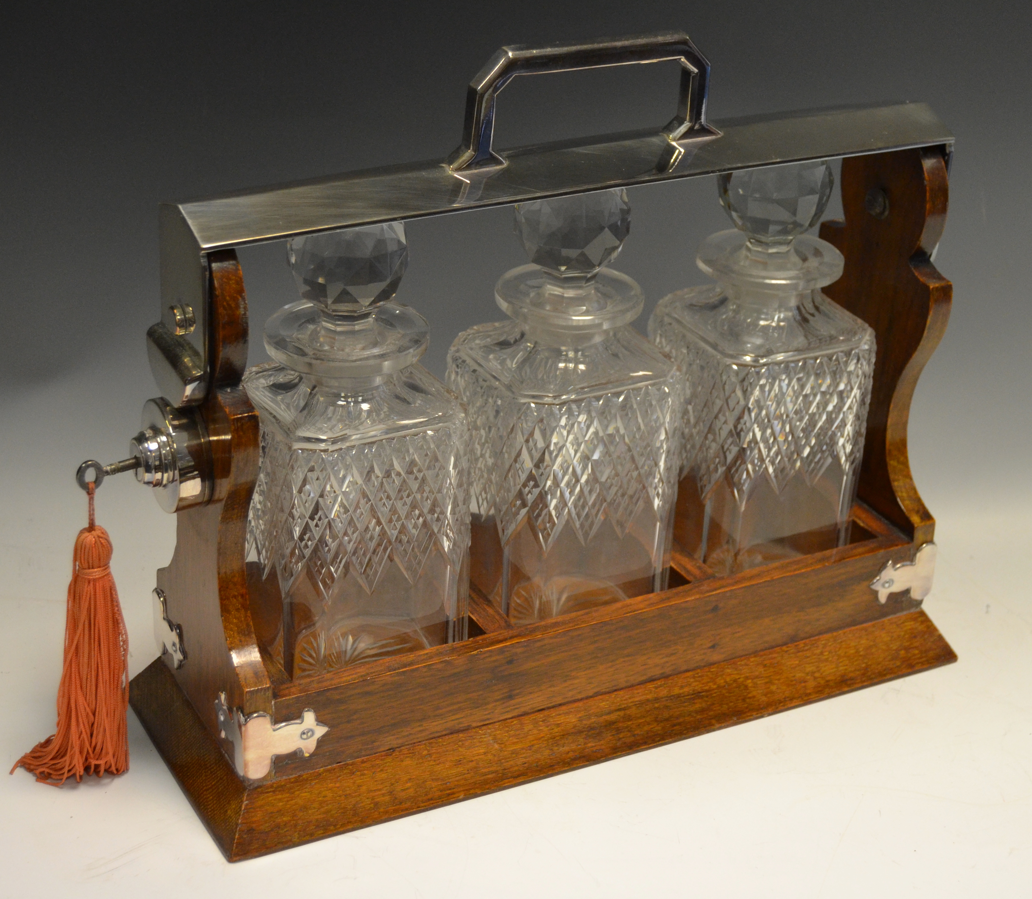 An early 20th century E.P.N.S. three bottle oak tantalus, hobnail bottles, prismatic stoppers,, c.