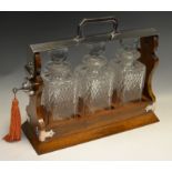 An early 20th century E.P.N.S. three bottle oak tantalus, hobnail bottles, prismatic stoppers,, c.