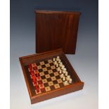 An early 20th century mahogany travelling chess set, plain bone with red stained opposition,