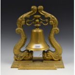 A countertop brass bell, gimbled mount between stylised fish supports, stepped base,