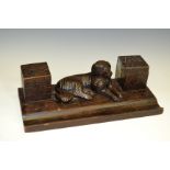 A late 19th century Black Forest two well standish, carved with a recumbent hound,