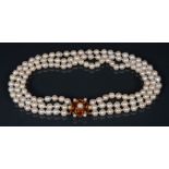 A cultured pearl triple strand necklace, orange paste floral centre, 9ct gold frame,