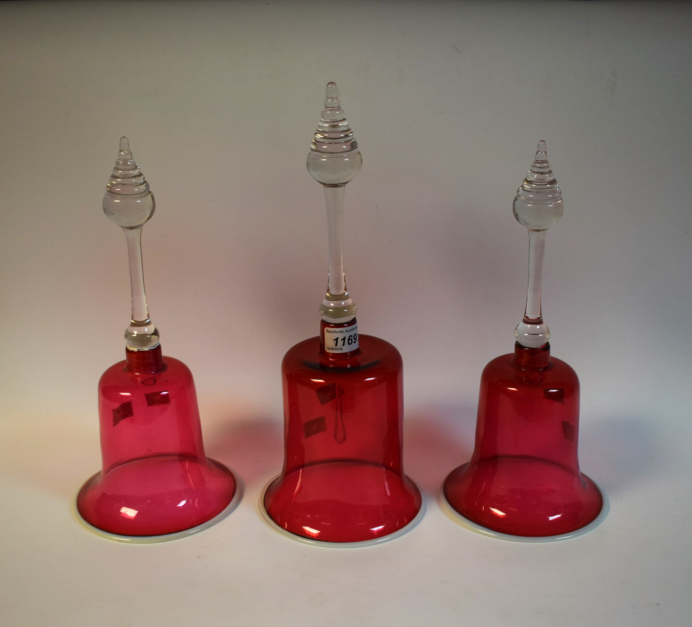 A pair of 19th century cranberry glass bells, white rims, clear glass handles, 32cm high; another,