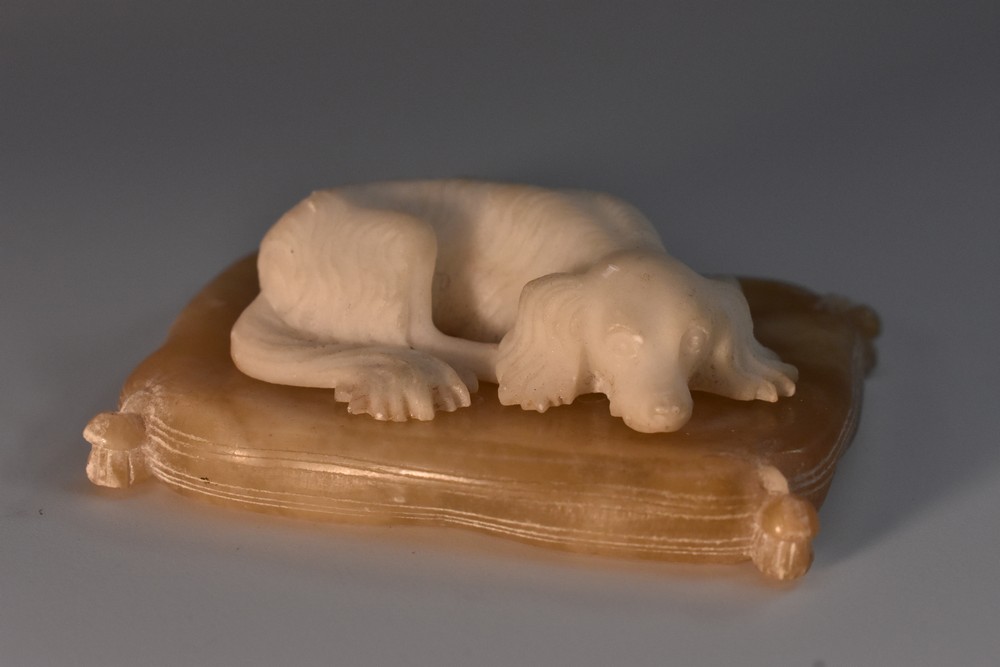 A 19th century alabaster model, of a King Charles spaniel, recumbent on a cushion,