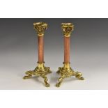A pair of late 19th century brass and copper Corinthian column tripod table candlesticks,