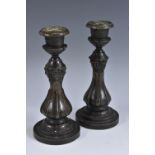 A pair of 19th century dark patinated bronze candlesticks, each cast with masks and lotus,