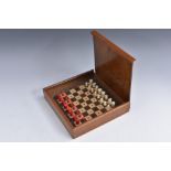 An early 20th century mahogany travelling chess set, turned bone pieces with red stained opposition,