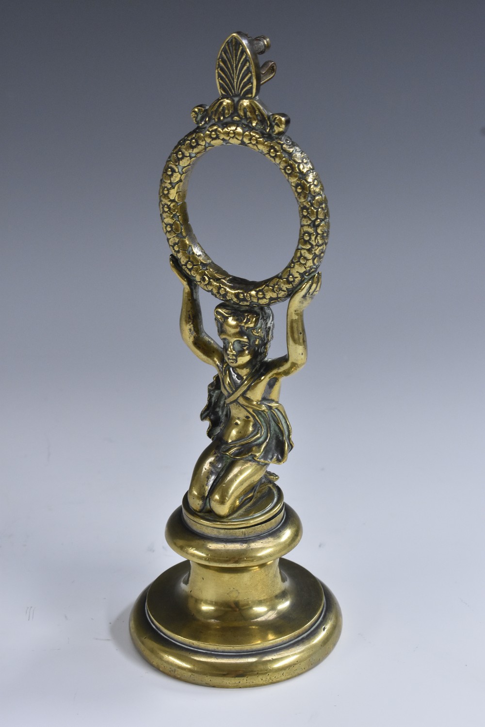 A 19th century brass pocket watch stand, as a scantily clad putto, kneeling, holding a chaplet,