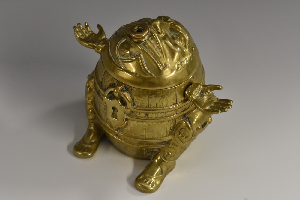 A 19th century brass novelty string box, as a comical figure trapped within a barrel,