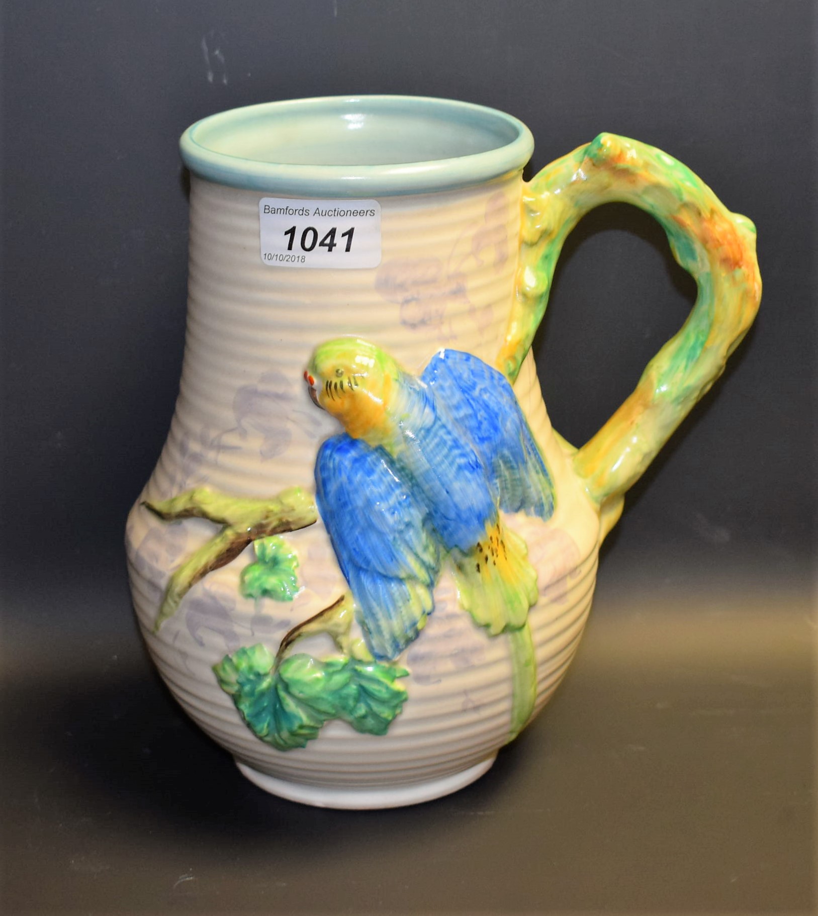 A Clarice Cliff jug, in relief with a budgerigar, in blue and green, rustic handle, 22.