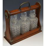 A Victorian oak three bottle Tantalus, moulded decanters and stoppers, 37cm wide, c.