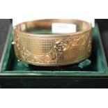 A 9ct gold hinged bangle, engraved with a wavy band of foliate scrolls on a hatched ground,