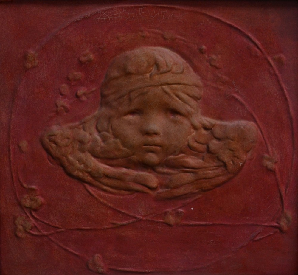 An Art Nouveau square plaque, moulded in high relief and centred by a mask of a putti,