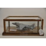 A HAND BUILT MODEL OF A HARRIER AIRCRAFT WITH PILOT IN A GLASS DISPLAY CASE ( VENDORS DESCRIPTION )