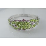 A silver hinged bangle set with rubies and peridot