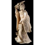 A Japanese carved ivory okimono: in the form of a bijin wearing a flowing kimono,