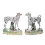 A pair of Staffordshire pottery Dalmatians: each standing before a stump in alert posture with