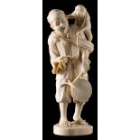 A Japanese carved ivory okimono: depicting a street musician holding a drum with a monkey on his