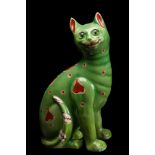 A Mosanic pottery cat: modelled seated and painted with red circle and heart motifs on a green