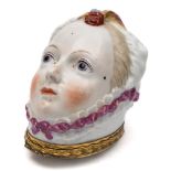 A Chelsea bonbonniere: modelled as a lady's head wearing a pink ribbon trimmed mob-cap with feather