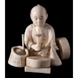 A Japanese ivory okimono of a seated merchant: in front of a mill stone with hammer in hand,