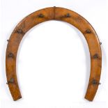 An early 20th century oak horseshoe shaped riding crop or gun rack:, with eight pegs, 74cm wide.