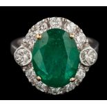 An emerald and diamond oval cluster ring: the central oval emerald approximately 12.5mm long x 9.