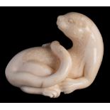 A carved fossilised marine ivory model of a sea otter: with raised head and curved tail, 8cm. long.