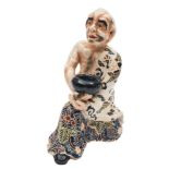 A Satsuma earthenware figure: of a kneeling bald headed monk, probably Daruma,