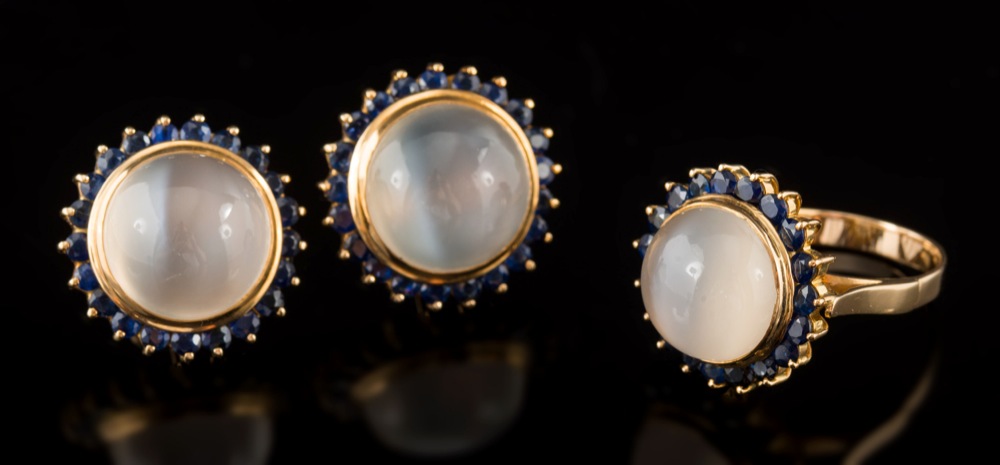 A pair of moonstone and sapphire circular cluster earrings: each with a single circular moonstone