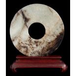 A Chinese jade bi-disc: of plain design with pierced centre and wood stand, 9cm. diameter.