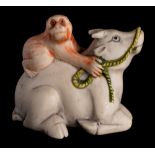 A Japanese carved and stained ivory netsuke: depicting a monkey seated on the back of an oxen,