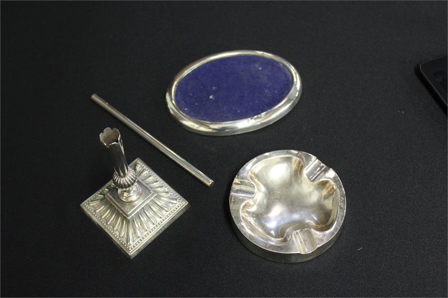 Silver, to include a silver ashtray, a silver frame, a silver tube and silver candle base, (4)