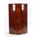 George III mahogany hanging corner cabinet, with a bowfront enclosing shelves