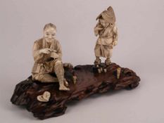 Okimono/Figurengruppe mit geschnitztem Holzsockel - "Rastender Krabbenfischer mit Frau", Figuren und