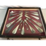 Collection of silver handled shoe horns displayed in a glass and wooden case.