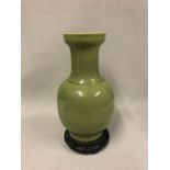 Oriental green glazed baluster vase with hard wood stand. Stands 32cm in height.