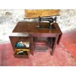 Cast iron base Singer sewing machine fitted within a wooden cabinet.