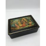 A Russian Lacquered box with hand painted figures to the top and signed by the artist. Measures 5.